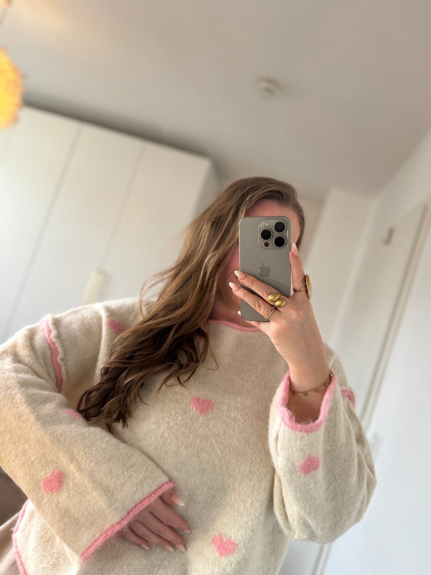 Model trägt einen beige-rosa Strickpullover mit zarten Herzchen und weicher Struktur, tragbar von 36 bis 42.